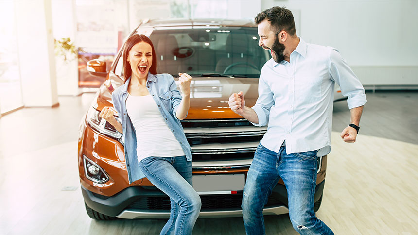 Two first-time auto buyers celebrating next to their car that they just bought.