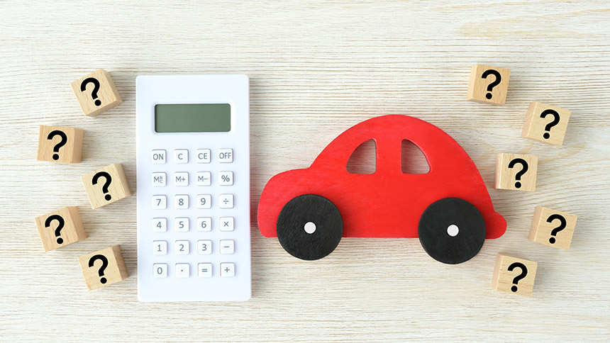 Wood blocks of question marks, a car, and a calculator on a table, symbolizing the true cost of owning a car.