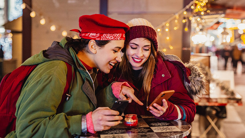 Two women in a store around the holidays looking for deals on their phones.