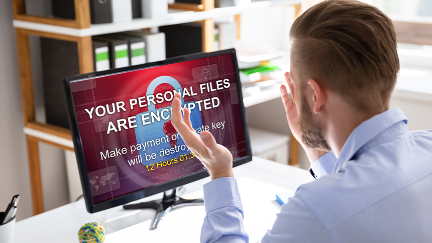 A frustrated businessman staring at a computer screen with a warning that his personal files are encrypted.