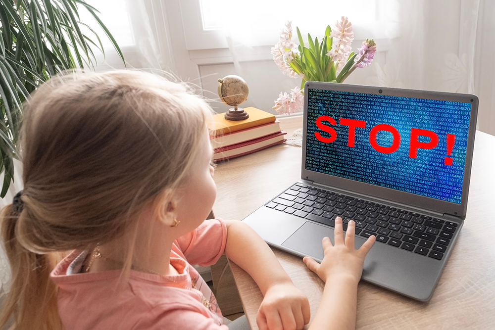 A young girl on a laptop with, "STOP," shown boldly on the laptop screen to represent cyber hygiene.