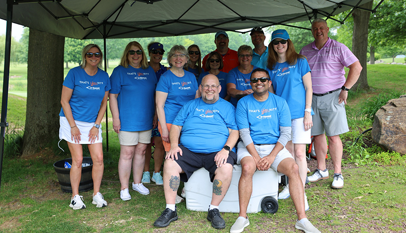 Diamond Named as One of the Best Places to Work in PA for 2025 A group of Diamond Credit Union employees are pictured out sided under an easy up tent. They are wearing their blue younity tshirts. Two men are in the middle sitting on a cooler with the rest of the group surrounding them as they smile and look at the camera.