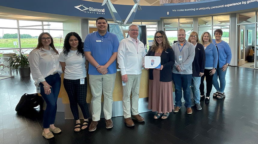 Nine Diamond Credit Union employees are pictured at the Wyomissing branch with the 2025 People's Choice Award certificate. The nine employees are standing in a line in front of the Service-First Desk. The fourth person from the left, DCU Sr. VP/Chief Member Experience officer, is presenting the certificate to Kaylee Rivera, DCU's Wyomissing Assistant Branch Manager.
