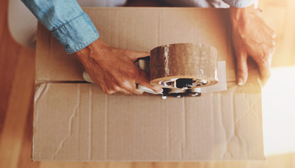 A person is taping up a brown moving box. Only the hands of them are visible as they tape up the box.