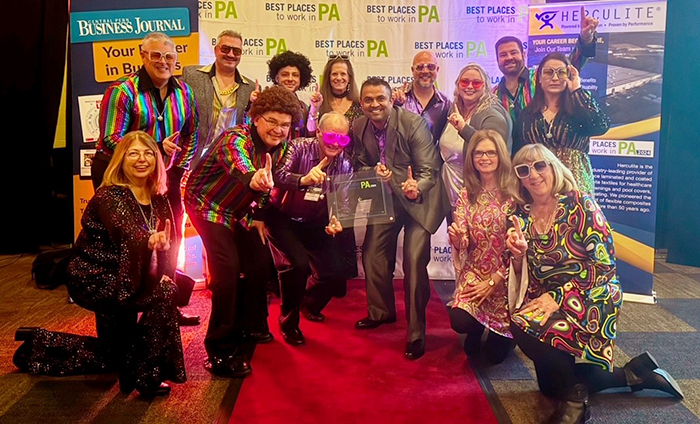 Fourteen members of the Diamond Credit Union team are pictured at the 2024 Best Places to Work awards ceremony and dinner. The team dressed in disco attire to take part in the theme of the event which was disco. Diamond's President and CEO, Rick Patel (center-right), and Diamond's Chairman of the Board (center-left), are in the middle of the group, holding the clear, square, best places to work award.