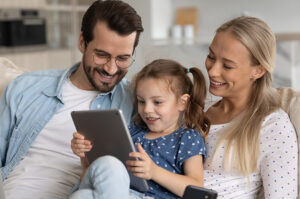 A mom, dad, and youth daughter smiling while looking at an iPad.