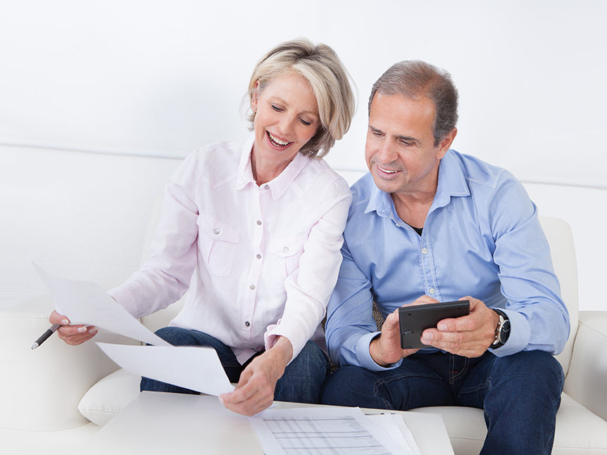 happy middle age couple looking at a paper and holding a calculator looking to reach a financial goal.