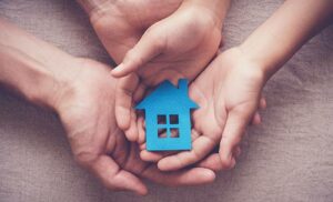 two sets of hands holding a small blue home figurine.