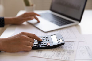 information request. person's hands touching a laptop mount and calculator which are sitting on a table.