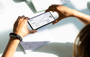 woman holding her phone over a check and taking a picture to represent mobile deposit capture.