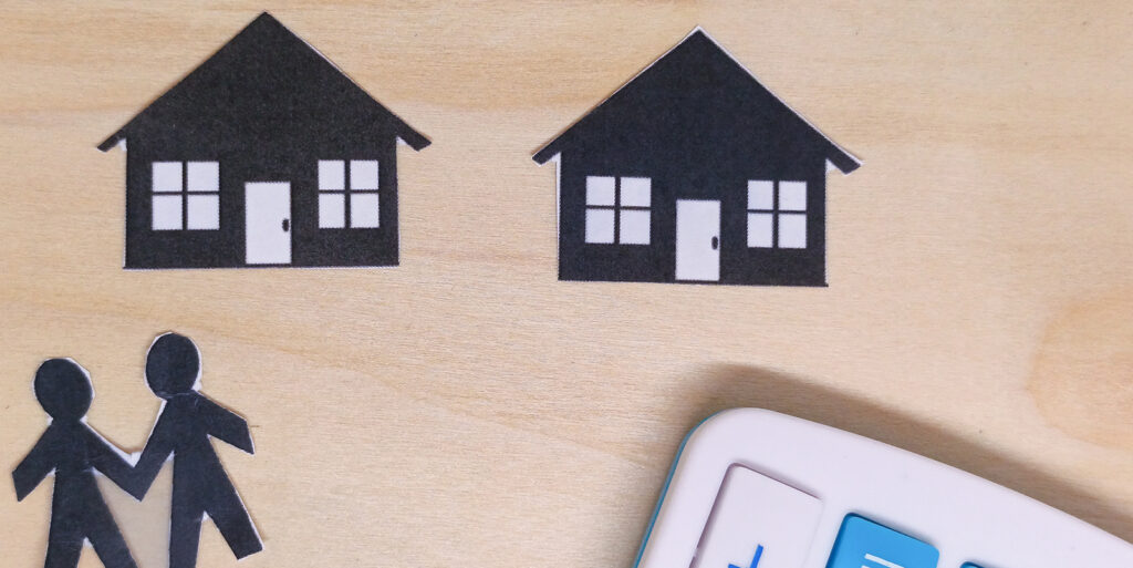 Paper cutouts of two houses and two people lay flat on a table. It's to represent unmarried couples buying a house.