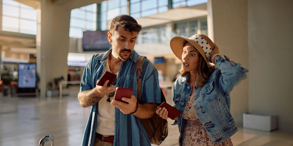couple at an airport looking at a phone wishing they knew how to avoid travel scams.