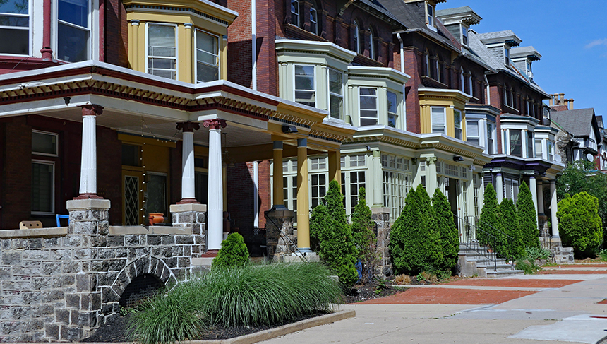 This photo represents the blog, "What is Escrow on a Mortgage Account?" It's a photograph of row homes on a street. The houses have bay window and front porches, The first house is red, then yellow, then two brick houses, another yellow house and then three brick houses.