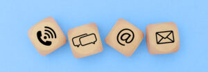 wooden dice with contact icons (phone, message, email, mail) on a blue background.