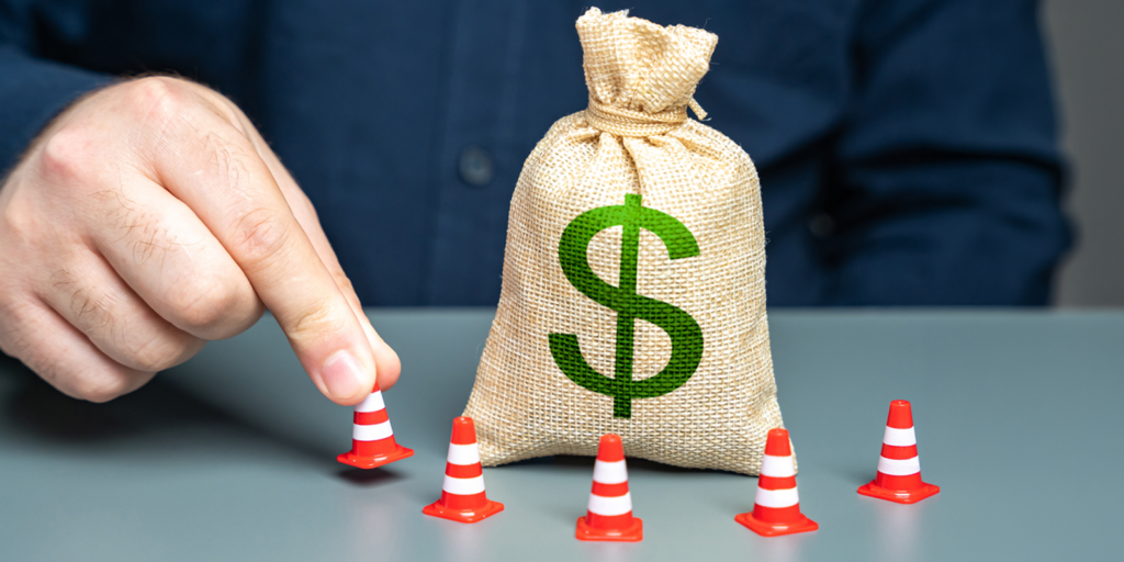 A man surrounds a dollar money bag with mini orange traffic cones representing setting financial boundaries.