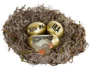 IRAs. Three golden eggs in a birds nest. One egg has coins and a dollar bill, one has the word "Roth IRA" and the the other has the word "IRA" on them.