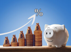 piggy bank next to an increasing stack of coins with money bags on it. above coins is an increasing arrow with a percent sign. signifies higher interest rate for a money market.