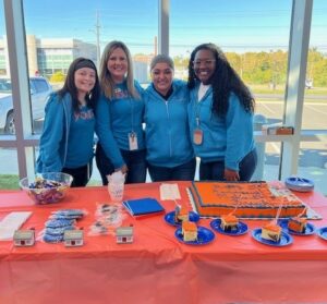 4 Tellers standing behind a table with cake and giveaways for their 5-year celebration. internship program