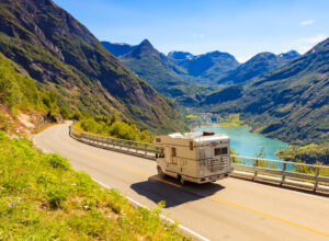 RV on a road with mountains and a lake in the background