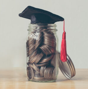 Clear jar filled with coins and a black graduation cap with a red tassel on top to represent scholarships. 