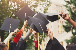 arms of 5 students holding their graduation caps in the air.