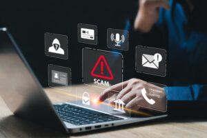 person sitting at a table with one hand on a laptop. identity theft/scam icons hovering above the laptop representing the importance of financial security.