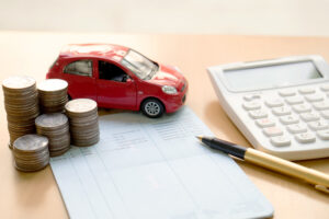 stack of coins, a red toy car, a pen, and a calculator sitting on a financial paper on top of a table.