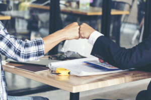 the arms of two people sitting at a table giving a fist pump. one person is part of a professional team, and the other is a customer.