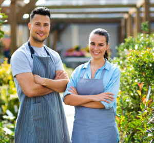 man and woman with arms crossed, smiling, wearing aprons and standing in a garden center happy with their choices of business checking accounts.