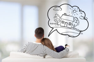 back view of a man with his arm around a woman sitting on a sofa with a dream cloud above drawing picturing a home with a fence.