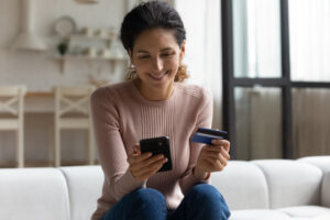 woman sitting on her sofa holding a credit card and smiling at her phone. Shows the ease of how to pay loans online.